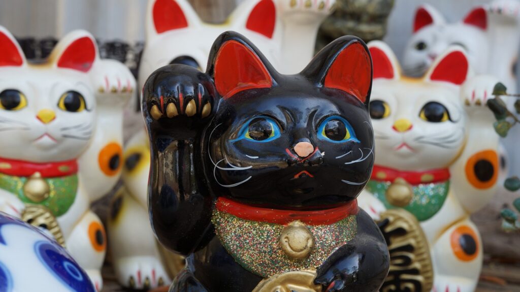 Glückskatzen: Schwarze und weiße Maneki Neko Figuren für Reichtum. Buchtipp: Der Almanach von Naval Ravikant.